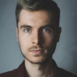 About Us Close-up portrait of a young man with facial hair and a serious expression.
